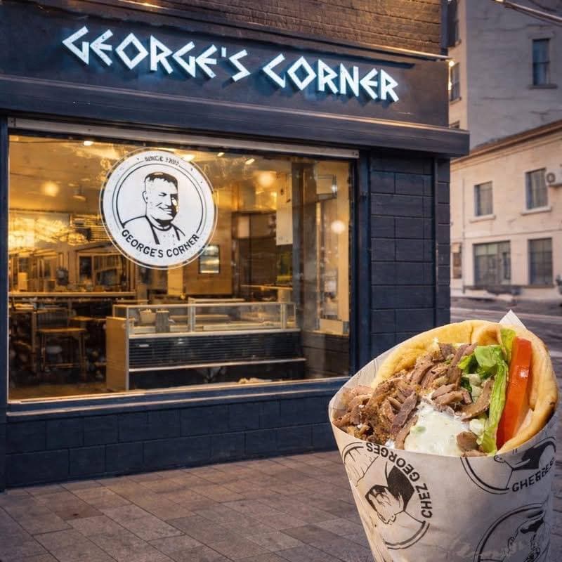 La devanture bleue de George’s Corner, enseigne allumée, un gyros dans son papier au premier plan
